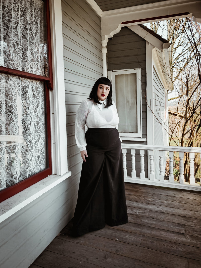 Elegant black Palazzo pants designed with a high-rise waist and flowing wide-leg cut, made from soft crepe fabric with minimal stretch, offering a comfortable yet polished look, and featuring two practical front pockets ideal for carrying small essentials while transitioning seamlessly from office wear to weekend outings.