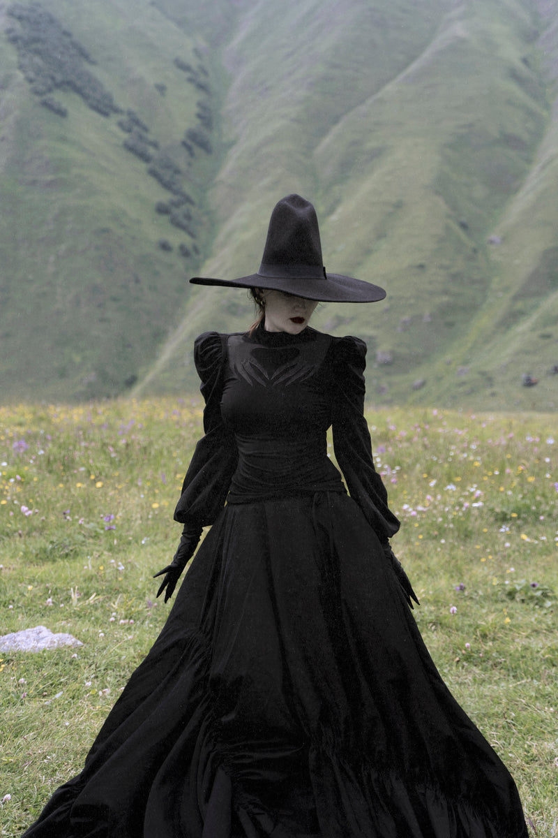 Black Phantom Blouse made with high-stretch polyester for movement and comfort, showcasing a sheer mesh chest cut-out with Naya’s haunting hand design, dramatic puff shoulders, and long gathered sleeves for a gothic, spellbinding style.