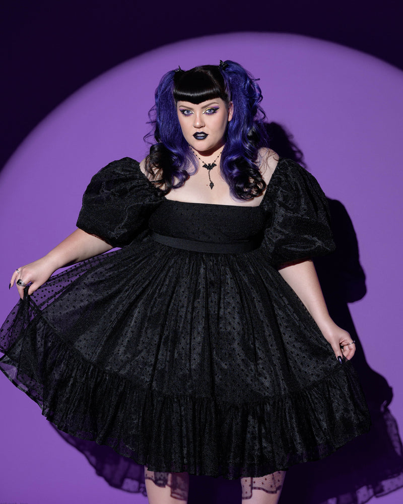 A beautifully detailed black polka-dot chiffon dress that exudes vintage and gothic elegance. Featuring a flattering empire waist, a square neckline, and dramatic puffed ¾ sleeves, this dress offers a charmingly poofy silhouette with its layered chiffon skirt that falls gracefully to the knee. Fully lined for comfort and quality, with a zip closure at the back, this timeless piece is ideal for springtime occasions, garden picnics, or alternative fashion wardrobes. 