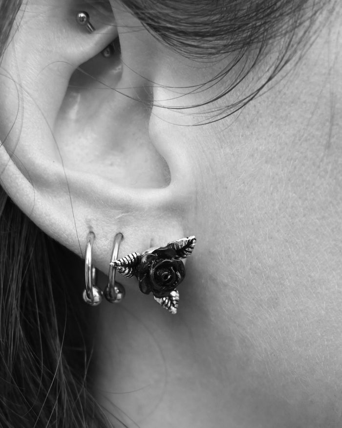 The Ring O’Roses Ear Studs showcase detailed black-rose blooms in fine English pewter and black enamel. Their gothic yet refined aesthetic embodies mystery and love, while the pewter offers comfort, shine, and resistance to tarnish. Compact and expressive, these ear studs bring a touch of dark sophistication to any outfit or jewelry collection.