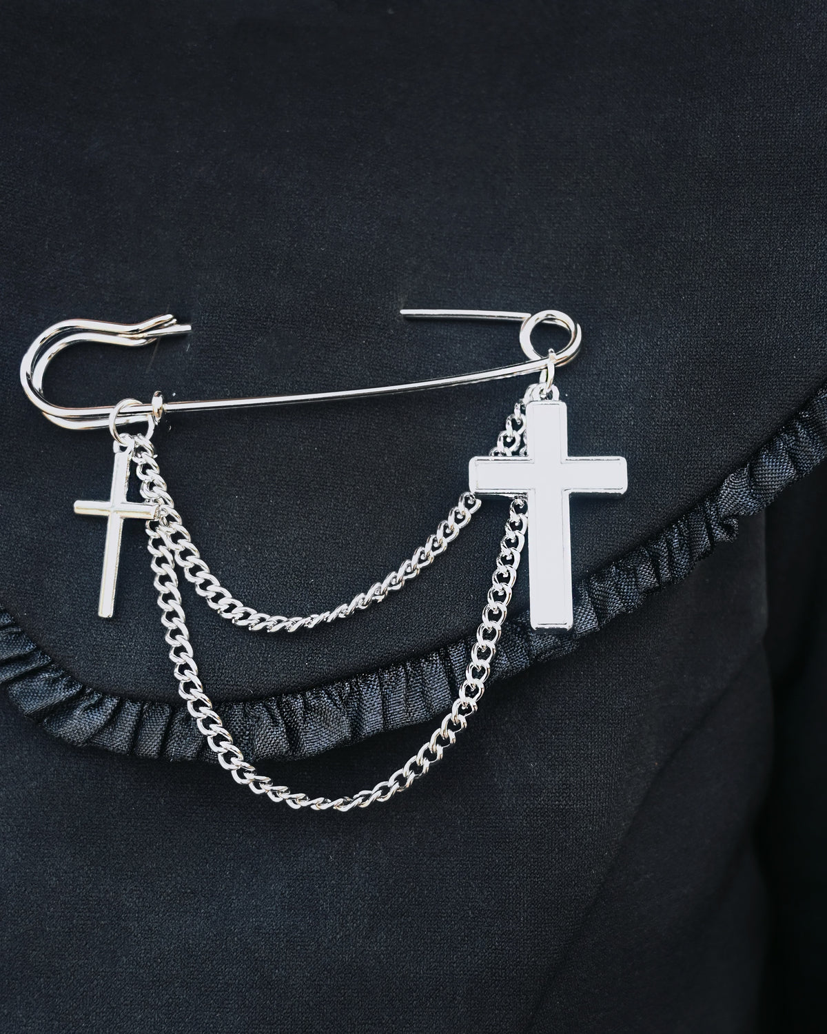 Silver oversized safety pin with dual cross charms and layered chain design. At 2.6 inches, this unique gothic-inspired accessory offers a sharp twist on classic jewelry, perfect for adding edgy sophistication to jackets, shirts, or handbags.