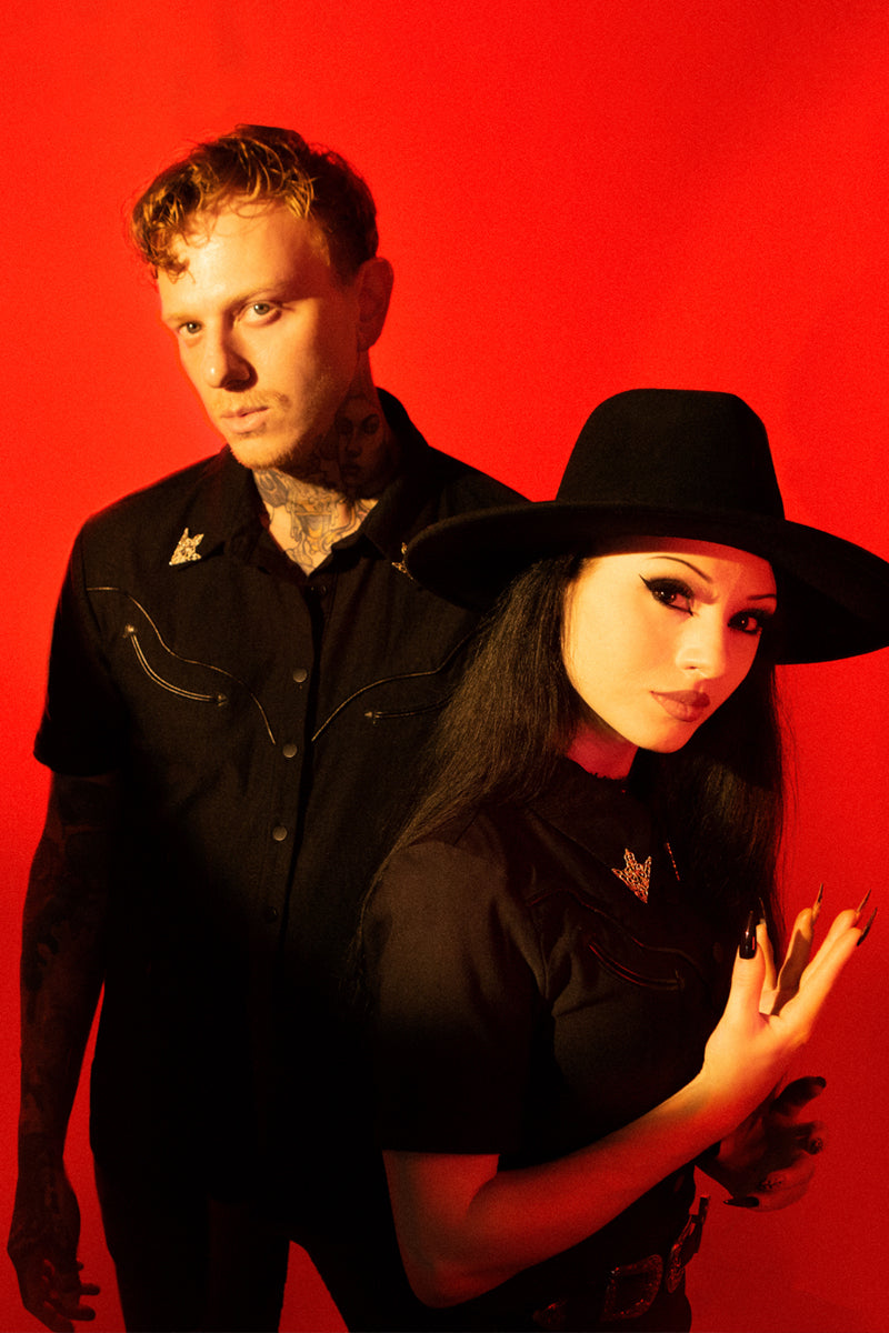 The Wayne Shirt is a modern gothic interpretation of timeless western wear, made from structured black bengaline that holds its shape beautifully while offering comfort and edge. Its striking vegan leather piping runs across the front and shoulders, emphasizing the tailored silhouette. With matte snap buttons that enhance its rugged aesthetic and detachable silver collar tips that allow customizable styling.