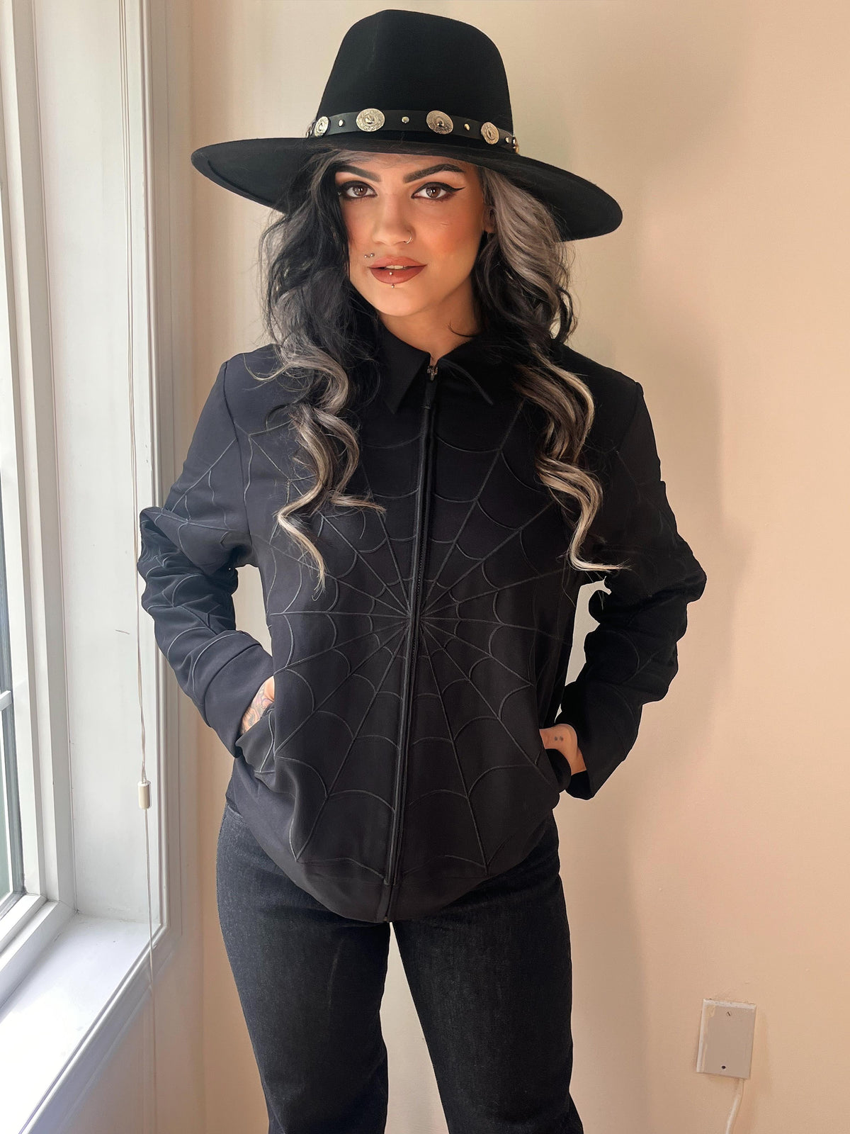 Retro-workwear style black jacket accented with black-on-black web embroidery spanning the body and arms, featuring dual side seam zip pockets plus a concealed internal pocket, marrying vintage aesthetics with modern functionality for fall and spring wardrobes.
