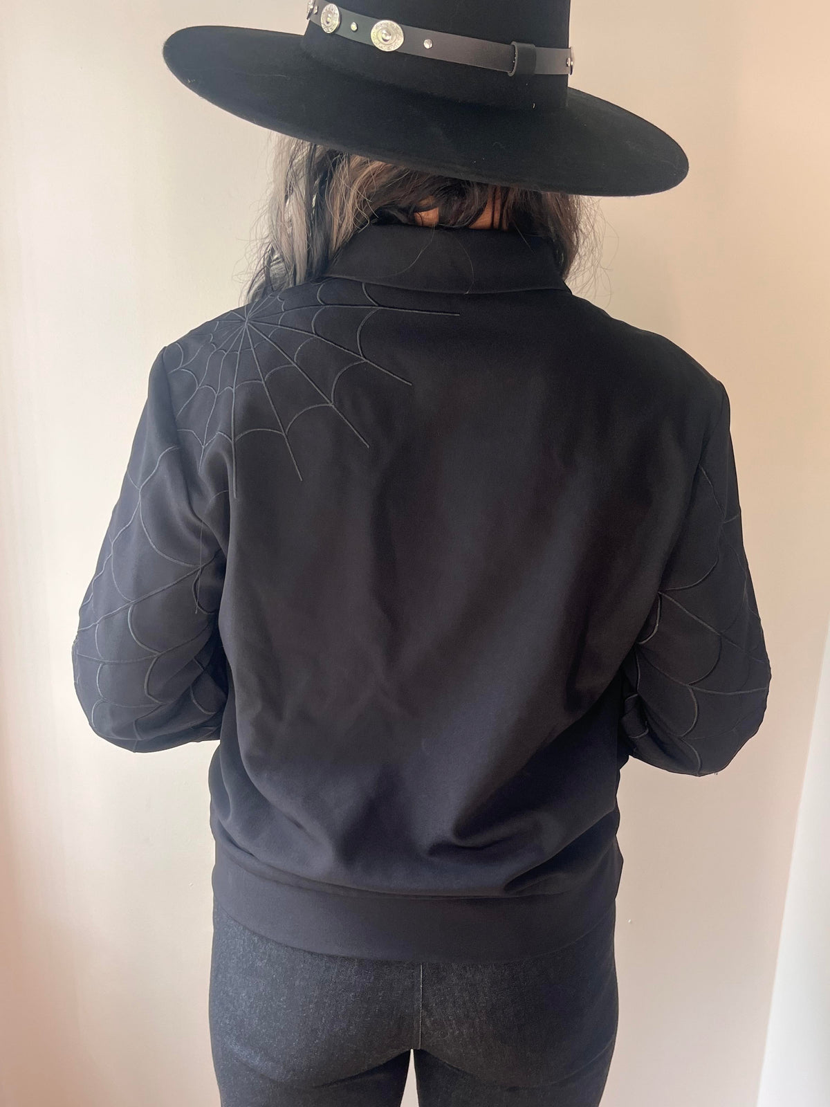 Black work jacket reinterpreting a 1950s dead stock prototype, adorned with black tonal web embroidery across front and back panels and sleeves, equipped with practical zip pockets on the sides and a hidden inside pocket—suited for transitional climate layering.