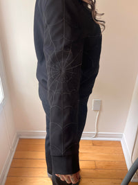 Utility-inspired black jacket channeling mid-century workwear heritage: black-on-black web embroidery decorating front, back and sleeves, two side seam zip-fastened pockets and an interior hidden pocket, designed to blend vintage styling and everyday practicality for cooler seasons.