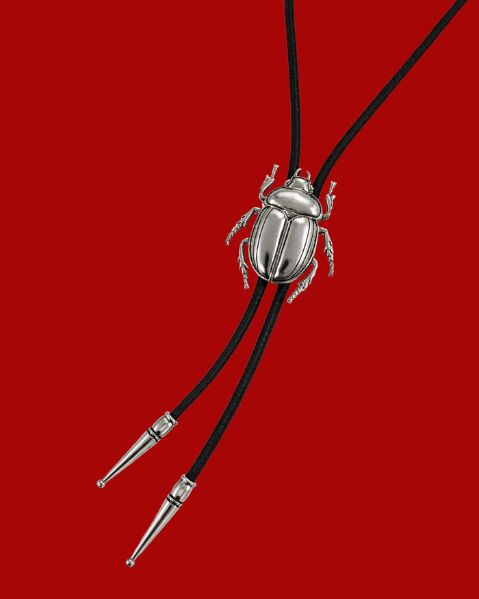 Silver beetle-shaped bolo tie on black cord against a red background