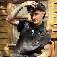 A gothic western bolo tie featuring a black coffin slide decorated with a white skull and bone-inspired design. The coffin slide is attached to a black braided nylon cord with tapered chrome-finished metal alloy spike tips for an edgy finish. Designed to adjust securely at the back, this retro bootlace tie adds a dramatic rock and roll touch to cowboy-inspired, gothic western, and teddy boy looks.