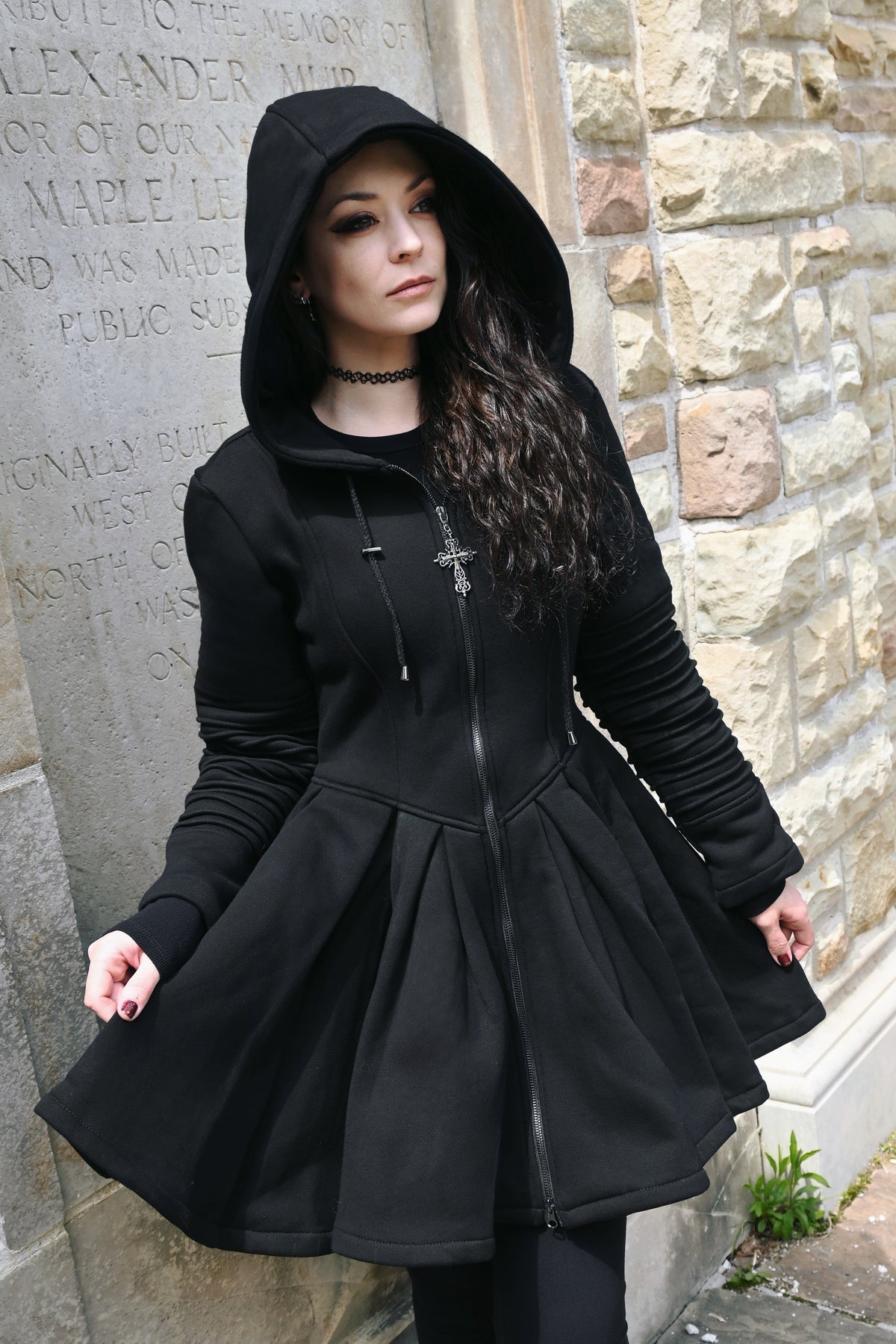 A dramatic black hoodie dress combining the cozy feel of an oversized sweatshirt with an elegant fitted silhouette. Crafted from thick 400 GSM 100% cotton with a soft fleece lining, the dress features a defined waist and full skater-style skirt. A deep hood and oversized pockets provide extra comfort, while the gothic cross zipper pull adds a distinctive dark detail to the design.