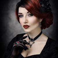 Woman with red hair and dark makeup wearing a black dress, gloves, and a necklace against a dark background.
