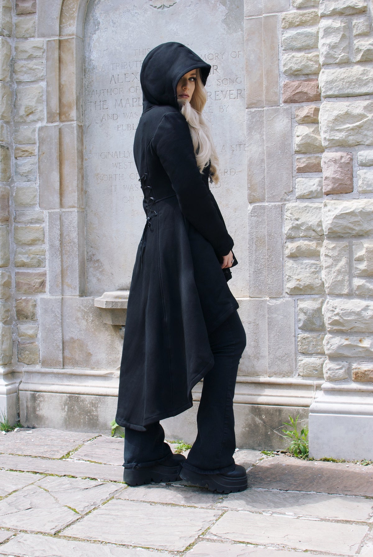 A dramatic black high-low hoodie made from heavyweight 400 GSM cotton with a thick, soft feel and warm fleece lining. The long silhouette features an oversized hood, deep pockets, and a black front zipper finished with a distinctive gothic cross zipper pull. Corset-style lacing decorates the back, adding a dark romantic touch to this cozy statement piece designed for colder seasons.