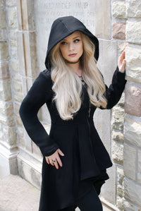 This black longline hoodie features a bold high-low silhouette, combining heavyweight comfort with dark romantic details. Constructed from 400 GSM 100% cotton, the garment has a thick, soft texture and warm fleece interior. An oversized hood and deep pockets provide cozy functionality, while corset-style back lacing and a black zipper with a gothic cross pull add striking alternative character.