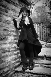 A statement black cotton hoodie designed for dramatic gothic layering, featuring a long high-low hem and oversized hood. The 400 GSM heavyweight cotton construction is thick, soft, and lined with warm fleece for added comfort. Corset-style lacing runs across the back, while deep pockets and a black front zipper offer practical details. The zipper is finished with an eye-catching gothic cross handle.