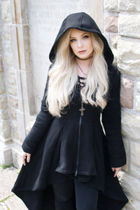A warm black high-low hoodie combining a dramatic silhouette with intricate gothic-inspired details. Made from 100% cotton in a substantial 400 GSM weight, it features a soft fleece lining, oversized hood, and deep pockets. Corset-style back lacing creates a distinctive structured accent, while the black front zipper is finished with a gothic cross-shaped pull. Ideal for cold-weather layering or standalone alternative styling.