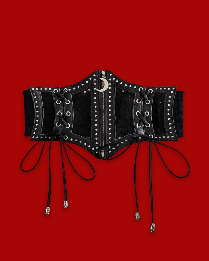 The Lunar Corset Belt features a dramatic black corset-style front crafted from synthetic leather with mesh paneling and silver-toned studs. A functional front zipper is finished with a crescent moon charm, adding a dark celestial touch. Decorative side lacing with silver skull aglets enhances the gothic design, while a wide ruffled elastic back provides a comfortable, flexible fit and defined waist.