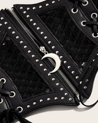 The Lunar Corset Belt creates a bold, waist-defining silhouette with its structured synthetic leather front and contrasting mesh paneling. Silver studs decorate the design, while a functional zipper pull featuring a crescent moon charm adds an eye-catching celestial detail. Decorative side lacing is finished with skull-shaped silver aglets, and the wide ruffled elastic back provides stretch and comfort.