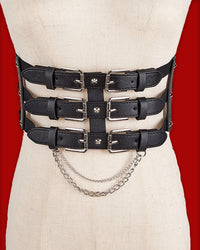 The Nocturne Harness Belt features a triple-tiered front made from structured black synthetic leather, detailed with six silver-toned buckles for a bold industrial look. Available in a classic version or with a detachable layered silver chain, it offers versatile styling options. A wide elastic back band provides a comfortable, cinched fit, while secure snap closures make it easy to layer over dresses, blazers, or oversized shirts.