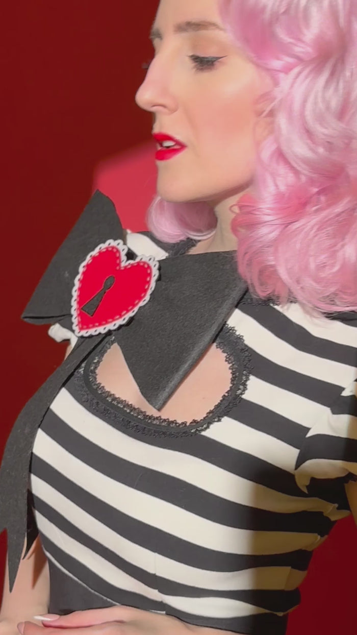 A stylish and body-contouring Molly Keyhole Dress designed by Jessica Louise, featuring a unique keyhole neckline, soft puff sleeves, and decorative ruffle trim. Constructed from premium stretch bengaline for both comfort and structure, this high-waisted dress highlights the wearer’s shape with a smooth, flattering fit. The look is completed with the brand’s signature Heart Bow, creating an enchanting combination of playful sweetness and confident sophistication—perfect for gothic and pinup.