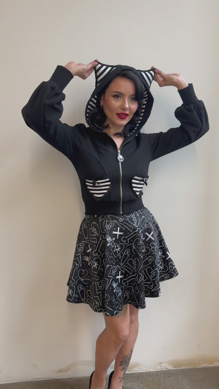 Black Meow Kitty Sweater showcasing puffed bishop sleeves, heart-striped pockets, striped puff cat ears, and signature skull zipper, designed to make a statement for scene fashion lovers and fans of iconic 2000s trends.
