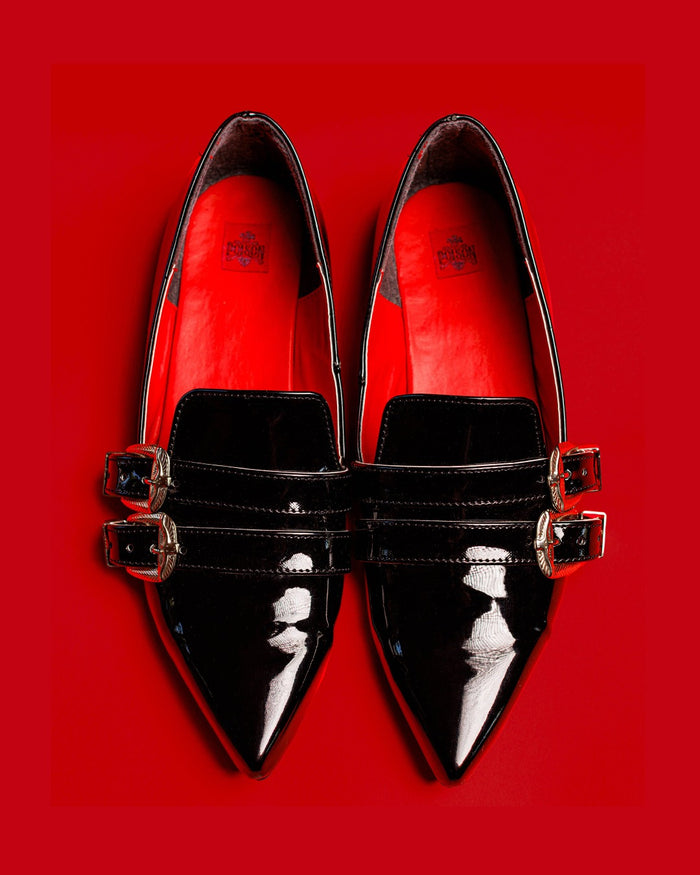 Top view of the Antonella flat shoes in patent black against a red background.