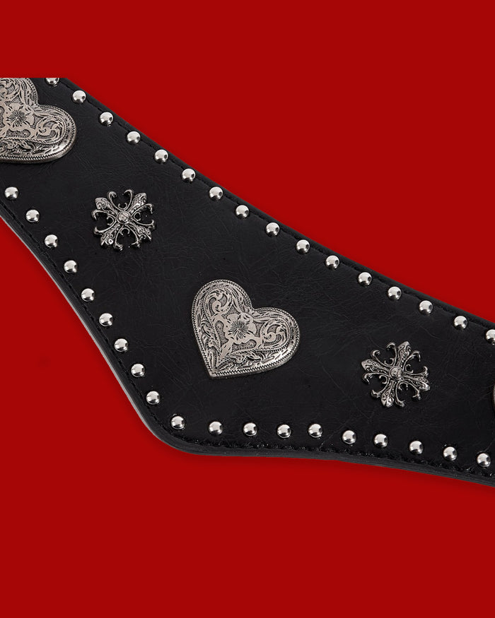 A bold western-style waist belt with a textured black synthetic leather front decorated with ornate silver-toned hearts and crosses. The Wild Heart Belt features a distinctive V-shaped silhouette designed to visually define and slim the waist. A wide stretch elastic back band offers comfortable movement and flexibility, while secure double snap closures make the belt easy to put on and wear.