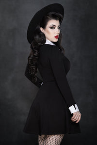 Model posing showing the back against grey background wearing Addams Dress, black hat and fishnets. 