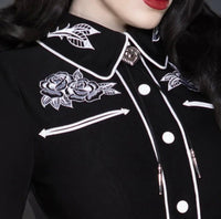 Timeless black and white June Carter–inspired dress made from high-quality stretch bengaline, showcasing crisp white piping and detailed floral rose and thorn embroidery for a bold, romantic finish. The figure-hugging wiggle design features long sleeves with piped seams, faux snap cuffs, and fixed front snaps for a sleek, seamless appearance — a perfect blend of classic femininity and modern edge.