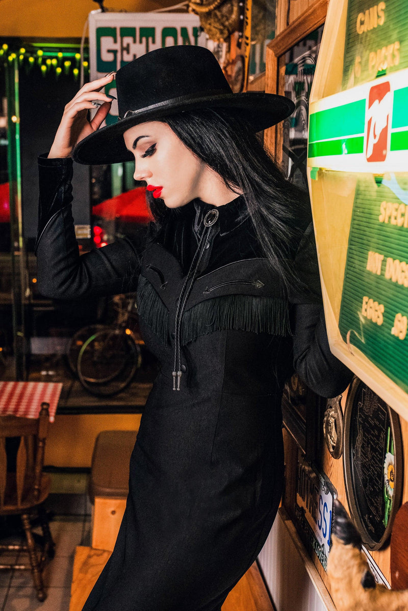The black Loretta Dress by Katakomb is a carefully handmade statement piece, featuring a playful cheeky fringe, arrow detailing along the bust, pleather yoke accents, and rich faux velvet panels, all created from high-quality bengaline fabric for a stylish, comfortable, and Western-inspired outfit.
