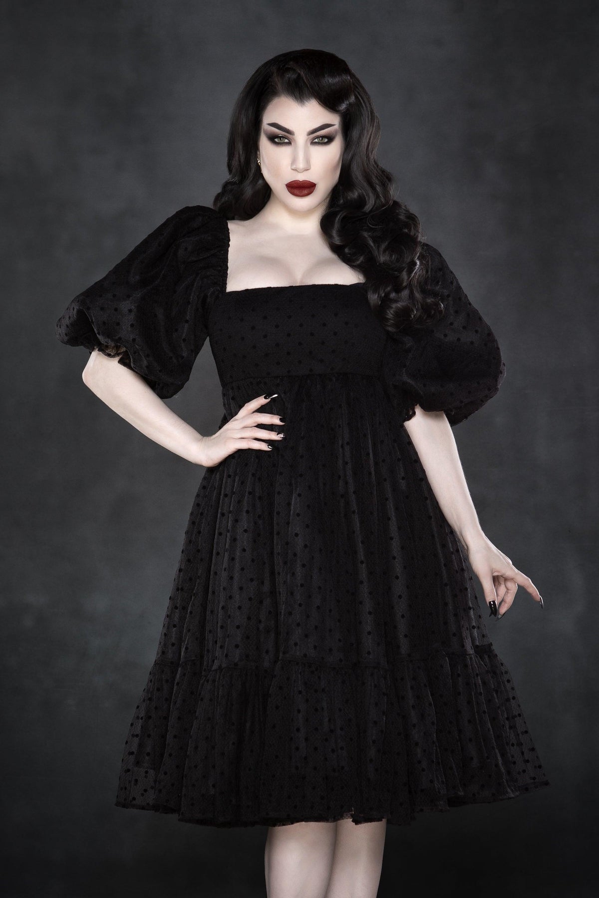 A romantic black chiffon dress adorned with classic white polka dots, designed with a square neckline and empire waist to accentuate a feminine silhouette. The dress’s ¾ puff sleeves and voluminous, multi-layered skirt create a dreamy, poofy look ideal for vintage or alternative fashion lovers. Fully lined for comfort and durability, with a concealed back zipper for easy wear. Made from chiffon and bengaline, this whimsical knee-length dress is perfect for springtime picnics and gothic garden parties.