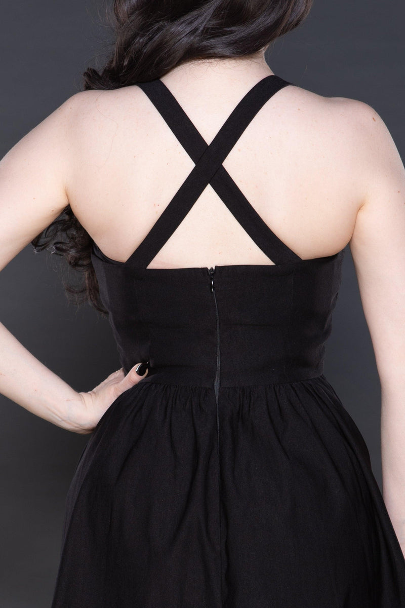 A contemporary take on the skater silhouette, this black dress built from smooth Bengaline fabric features bold criss-cross straps framing the upper body, a poised bodice flowing into a flared A-line hem, intricate front-panel embroidery with an almost hidden effect, and statement webbing buckles at the waistline that bring texture and edge to the overall look.