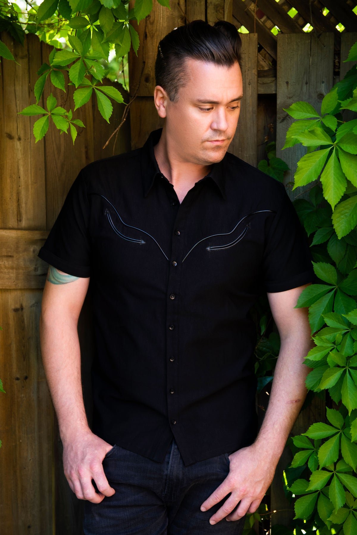 A fusion of gothic attitude and western heritage, the Wayne Shirt features strong tailoring in structured black bengaline with vegan leather piping that traces the iconic cowboy yoke. Matte snap buttons line the placket for a utilitarian touch, while removable silver collar tips give wearers the choice between understated refinement and dramatic metallic detail. This piece captures the essence of contemporary dark fashion—perfect for gothic cowboys and alternative style enthusiasts.