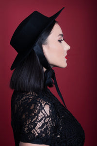 A model posing in side profile against a red backdrop while wearing the American Gothic mini hat in black.