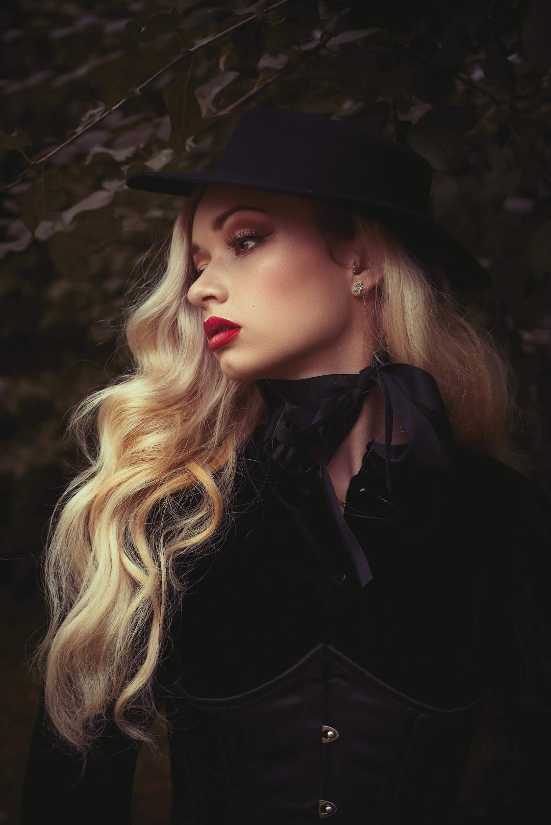 A pinup model posing in side profile in front of a tree while wearing the American Gothic mini hat in black.
