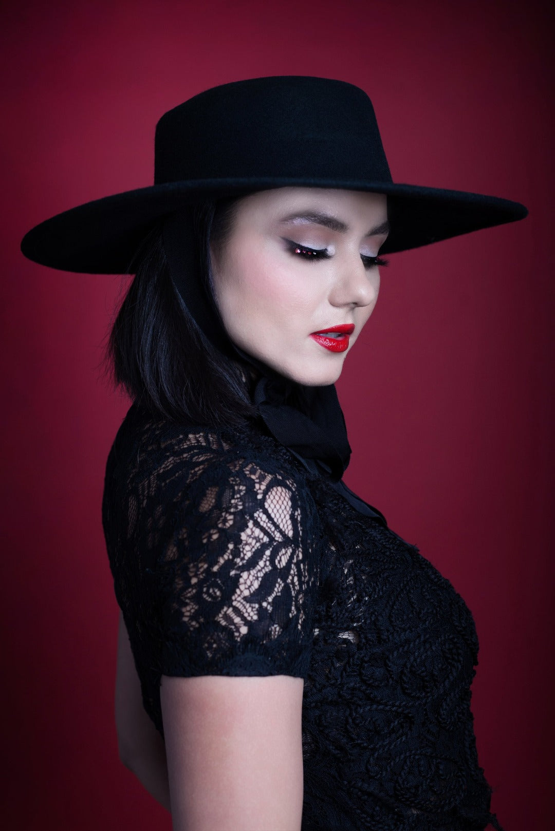 A model posing in side profile against a red backdrop while wearing the American Gothic wide brim hat in black.