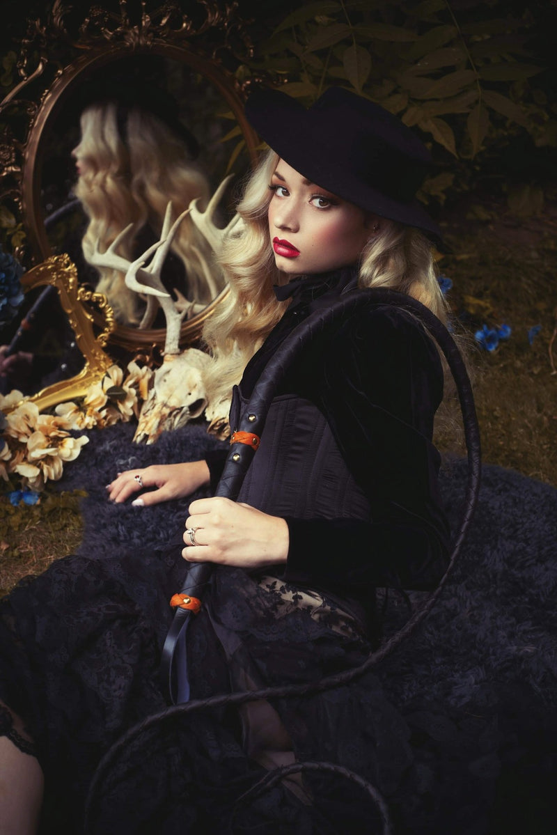 A pinup model posing in side profile sitting on grass while wearing the American Gothic mini hat in black.