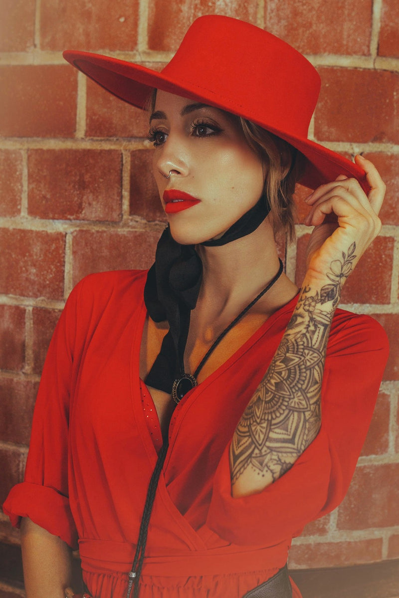  Pinup model posing against a red brick wall wearing a red, wide brimmed, wool hat.