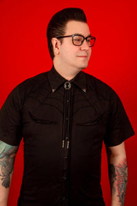A black western shirt featuring intricate black-on-black spiderweb embroidery on both the front and back. The Spiderweb Black Western Shirt is crafted from a comfortable cotton-poly blend and finished with contrasting black snap buttons that complement the dark monochrome design. Its combination of traditional western styling and subtle spiderweb details makes it a distinctive choice for gothic, alternative, and spooky western outfits.
